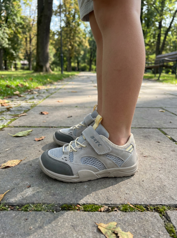 Nogi dziecka od kolan w dół w szarych butach barefoot Bartek na kamiennym chodniku — widoczna płaska podeszwa zero drop