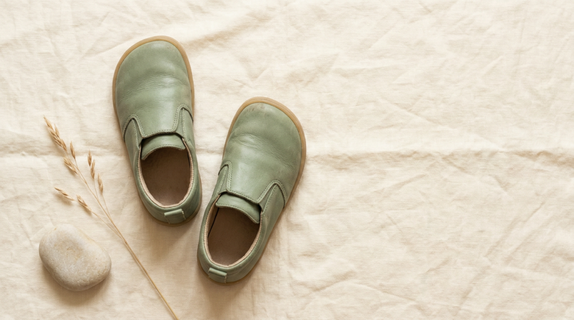 Dziecięce buty barefoot na lnianej powierzchni — widok z góry przedstawiający płaską podeszwę i szeroki nosek