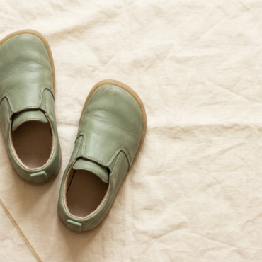 Dziecięce buty barefoot na lnianej powierzchni — widok z góry przedstawiający płaską podeszwę i szeroki nosek