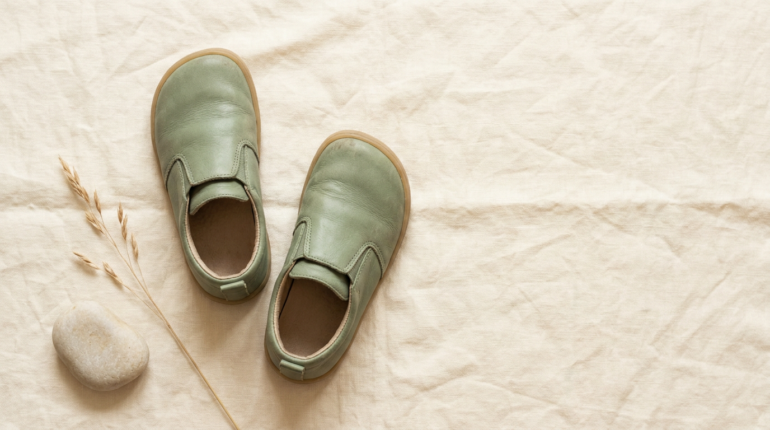 Dziecięce buty barefoot na lnianej powierzchni — widok z góry przedstawiający płaską podeszwę i szeroki nosek