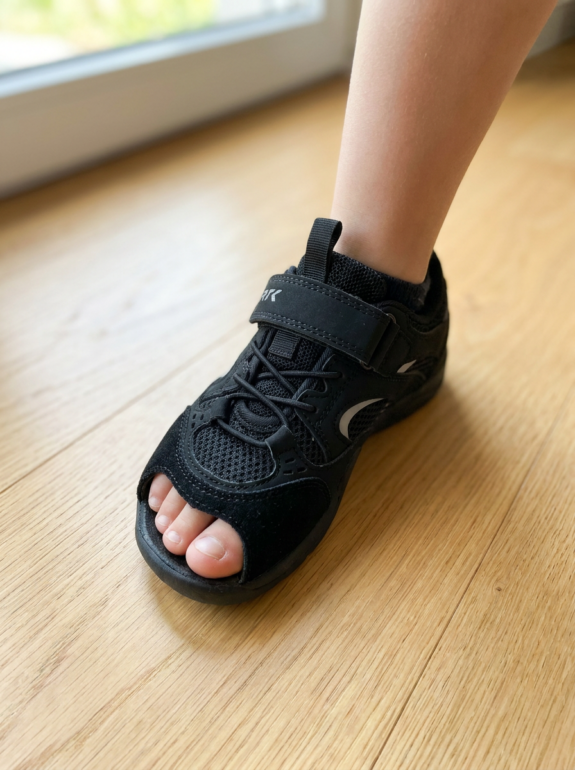Stopa dziecka w czarnych sneakersach barefoot Bartek — widoczna przestrzeń przy palcach i szeroki nosek buta